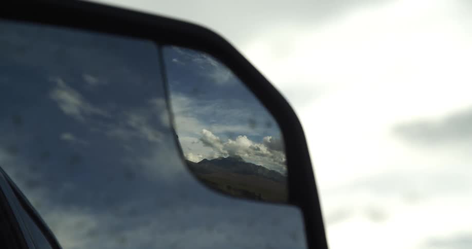 Clouds in the blue sky reflection on the rearview mirror of a moving car