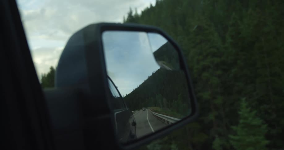 A car wing mirror of a car traveling on a highway next to a mountain