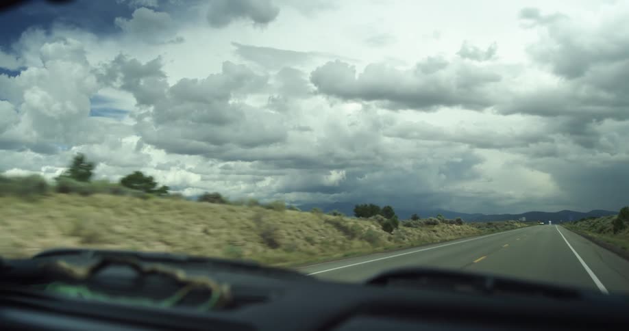 A car traveling on a desert highway on a cloudy day