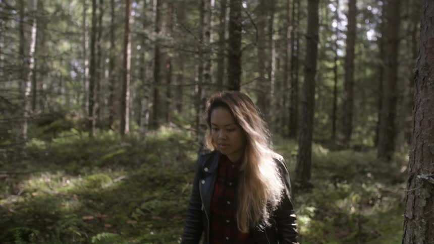 A woman walks through the woods and picks something and puts it in a red bowl