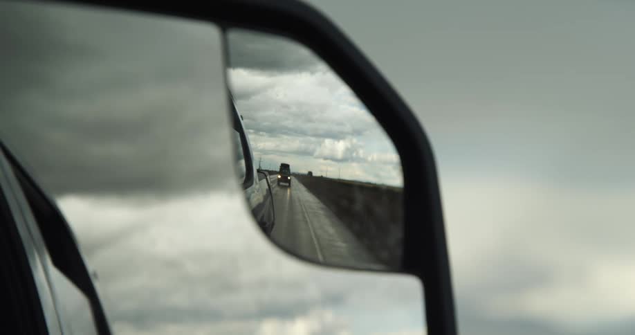 A reflection in the side mirror of a car traveling down a rainy road