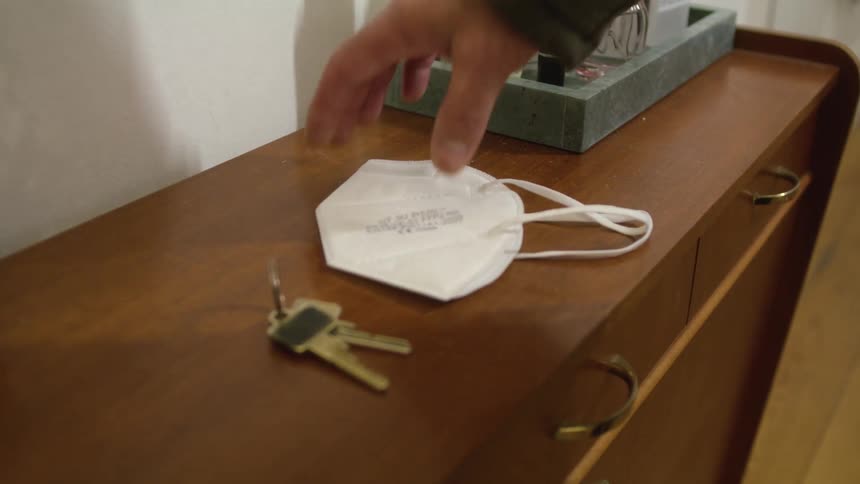 A man grabs his car keys and mask off the dresser