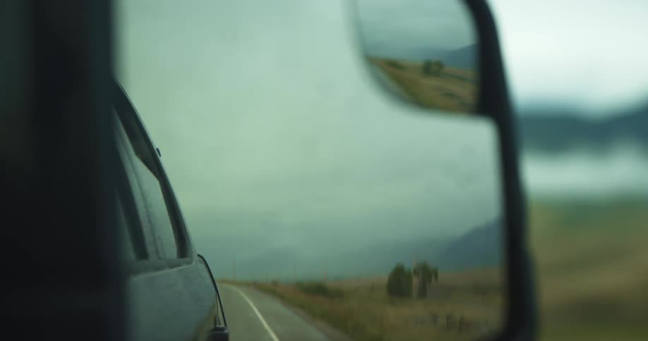 A vehicle with a rearview mirror driving on a road with the sky and clouds in the background