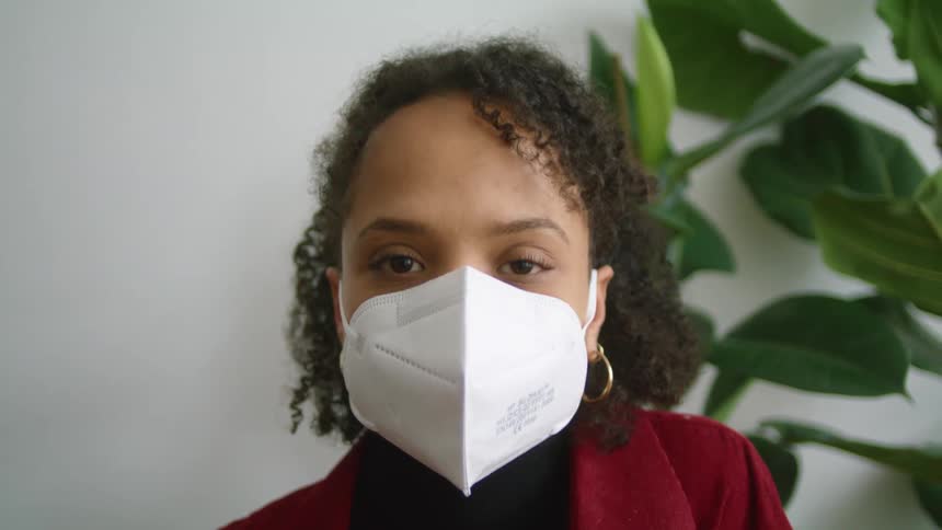 Woman wearing red jacket puts on face mask then smiles