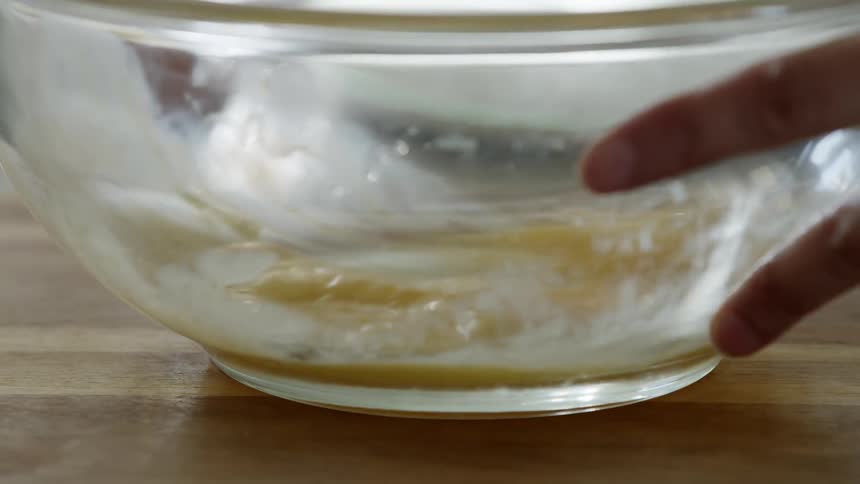 A woman at home beats eggs in a bowl with a whisk