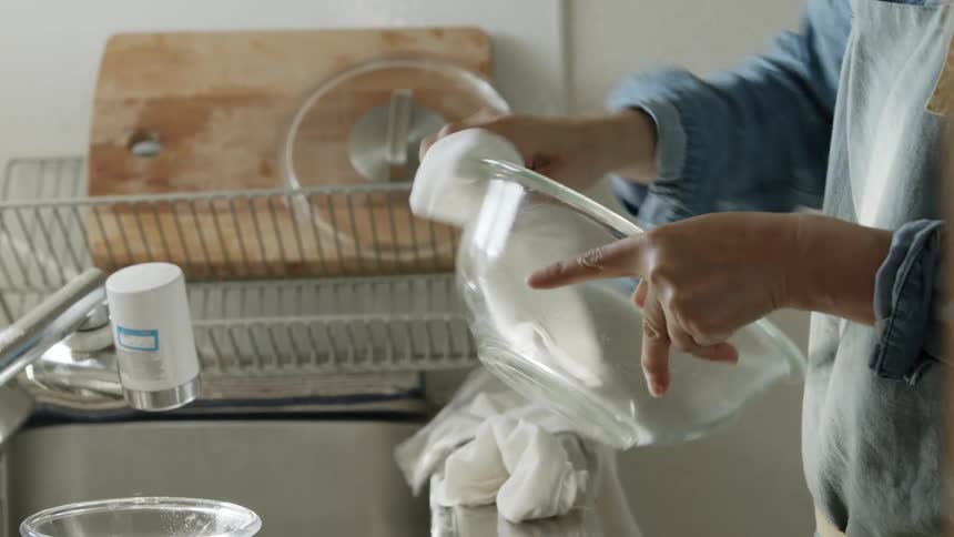 Man cleaning a glass mixing bowl with a dry cloth in the kitchen at home