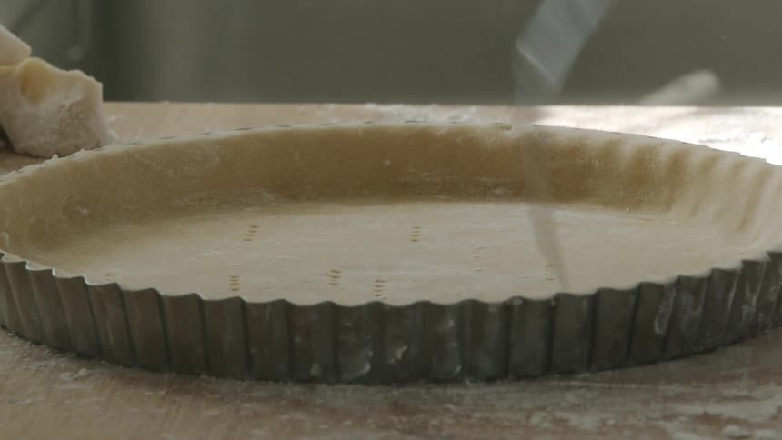 A baker uses a fork to pierce a tart before baking