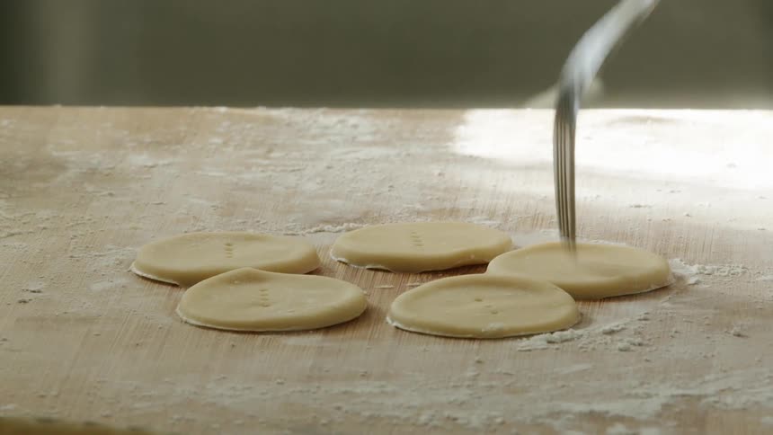 A person baking at home pokes pastry dough with a fork