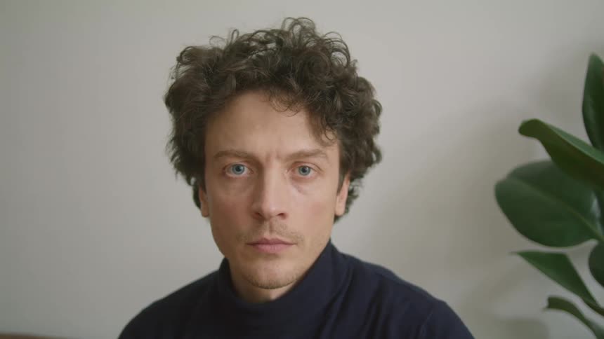 A man is sitting indoors next to a plant
