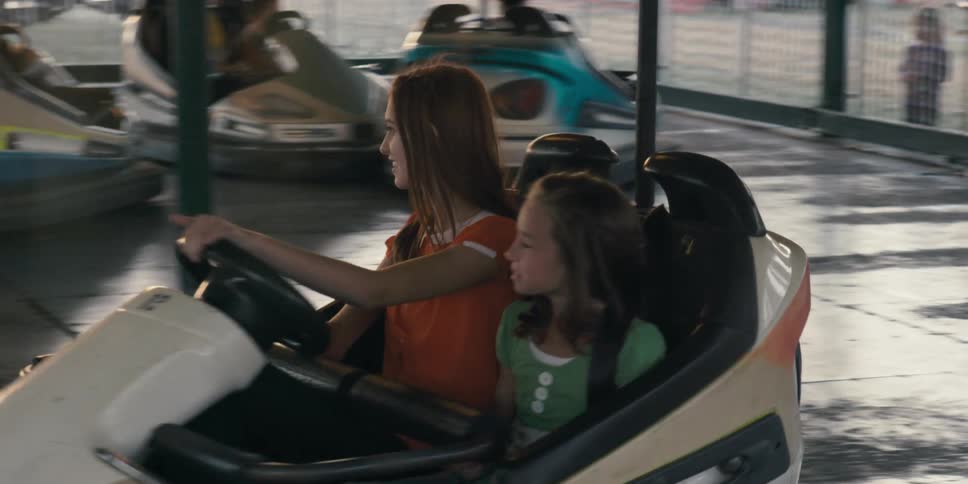 A young woman and girl ride together in a bumper car at a theme park attraction during the day