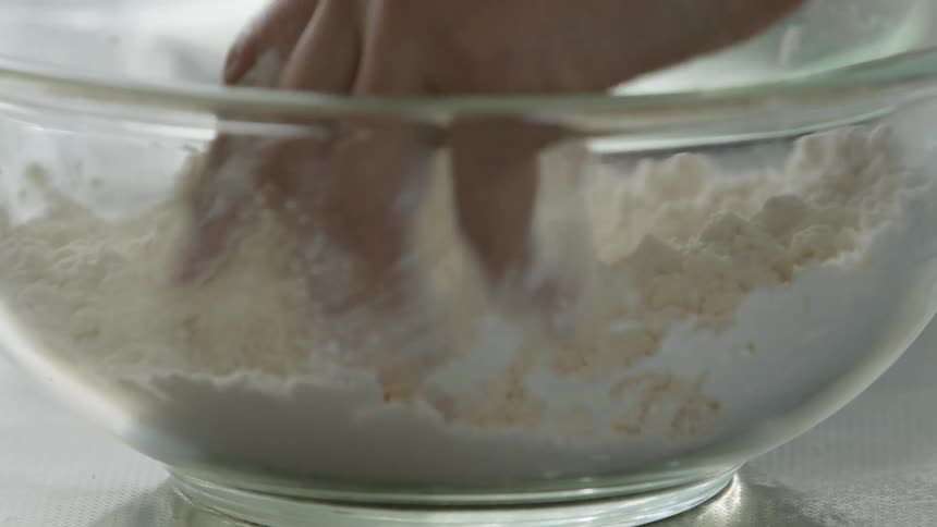 A person is breaking up powder in a bowl with their hands