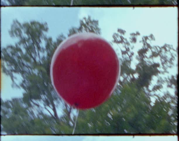 Red balloon on a string swaying back and forth outdoors