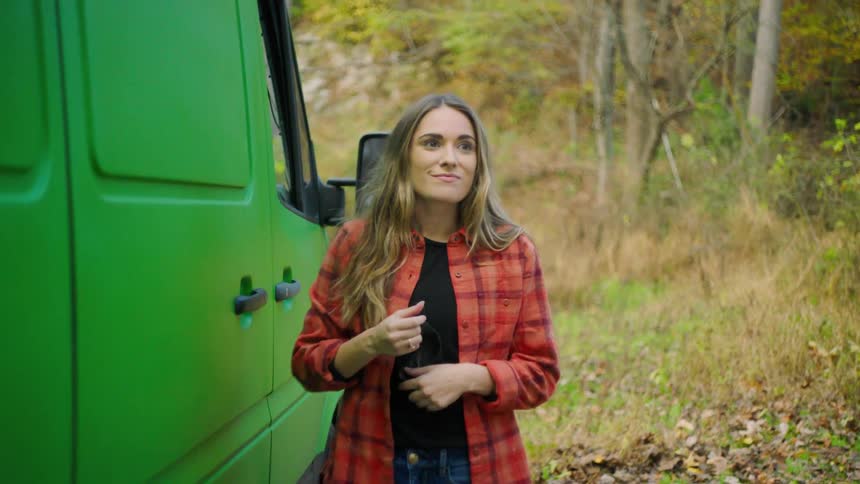 Woman shuts door of vehicle and removes mask to look around woods and smile