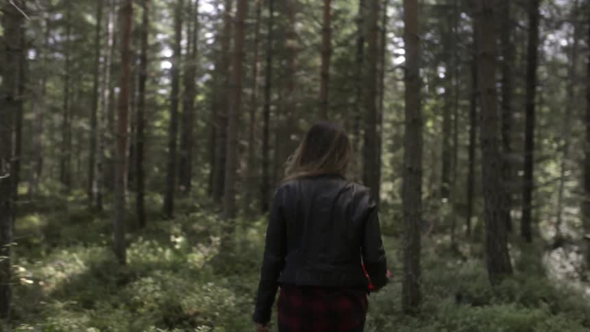 A woman wearing a leather jacket walks in a forest