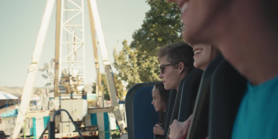 Men and women in amusement park ride with trees the sky and clouds in the background