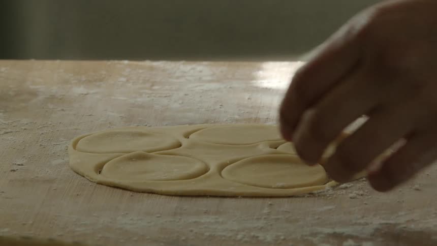 A woman at home uses a mug to cut cookies out of dough