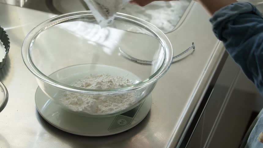 A person dumping flour into a mixing bowl