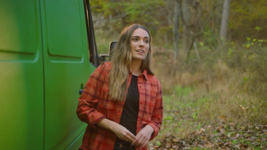 A woman gets out of the passenger seat of a green van and smiles as she closes the door