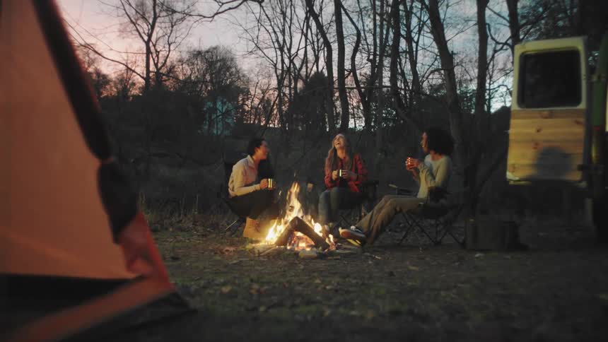 Three female friends chatting around a fire while camping in nature