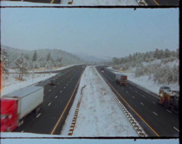 Trucks driving down the highway next to the pine forest on the hills at winter