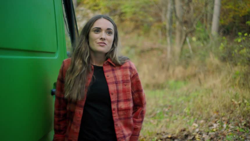 A woman shuts the door on a vehicle and smiles as she breathes in the forest air