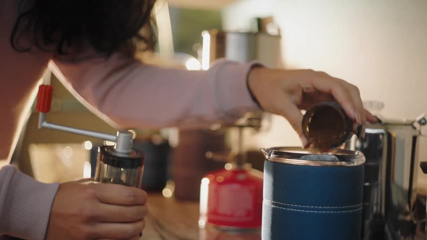 Woman pours freshly grounded coffee from the grinder into a container on the kitchen countertop