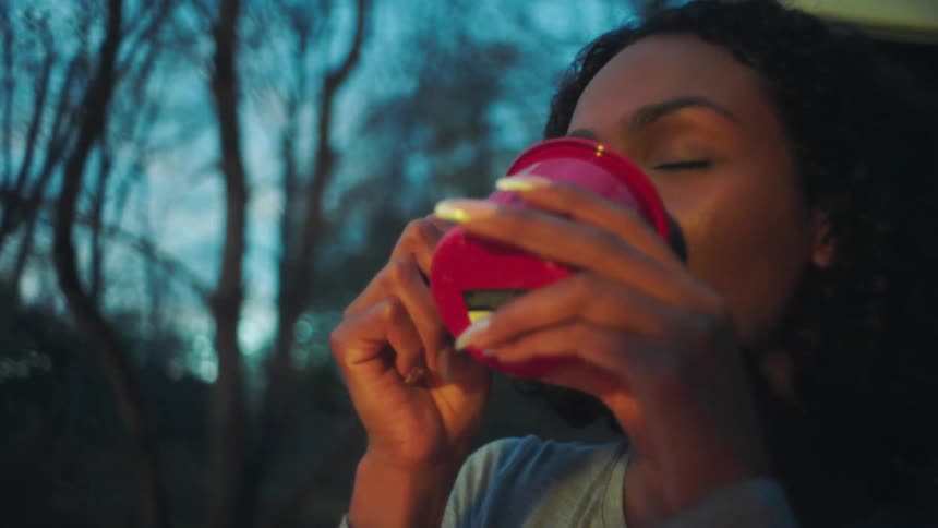 Female friends sitting around a campfire at evening enjoy hot beverages