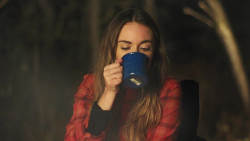 A woman sitting on a camping chair with smoke in the foreground and trees in the background