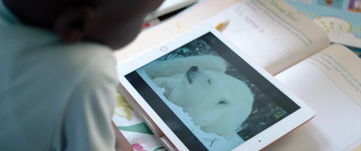 Young boy watching a video on a tabled placed over a book