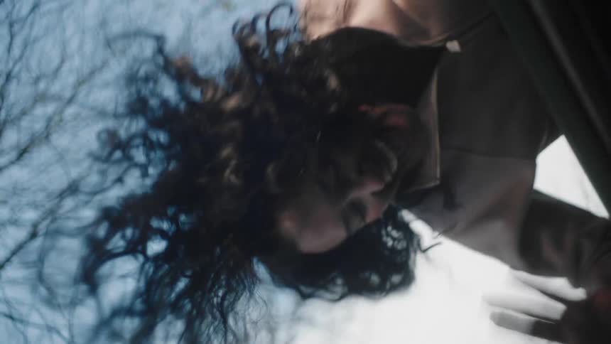 A woman climbing on top of a vehicle with trees the sky and clouds in the background