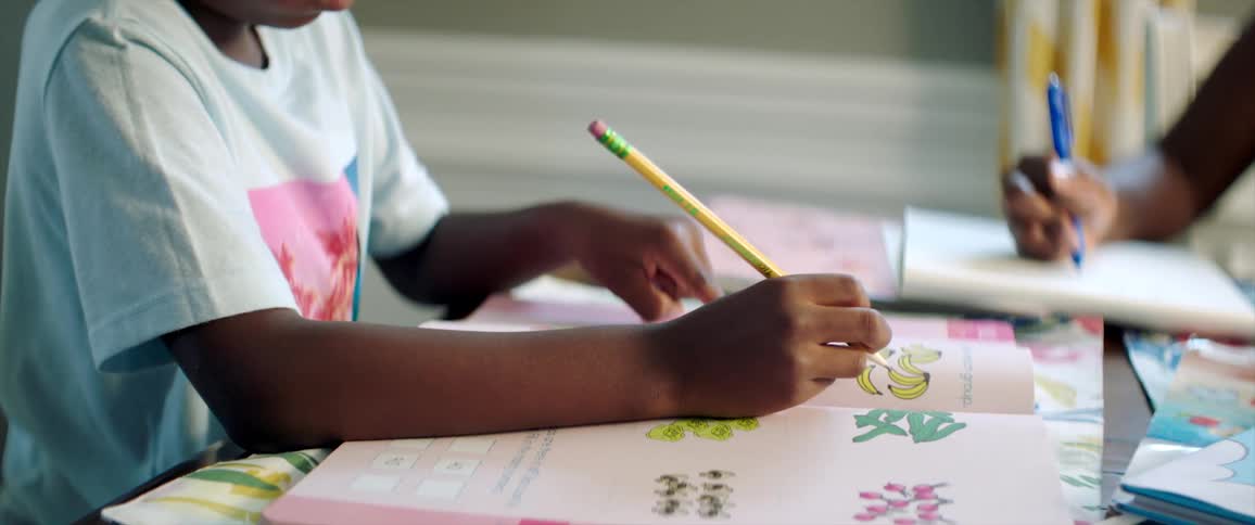 A boy sitting at a table holding a pencil and reading a book
