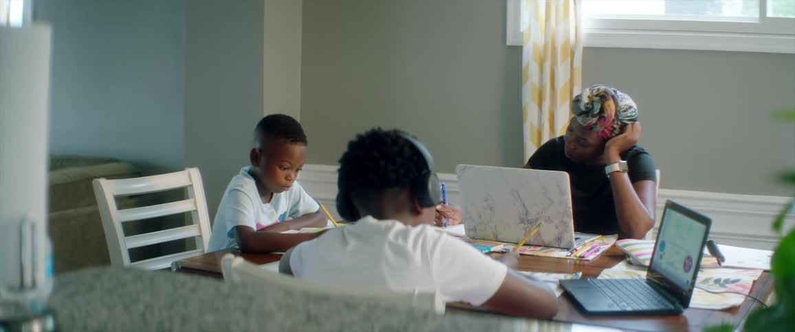 Mother takes notes from laptop as children do homework