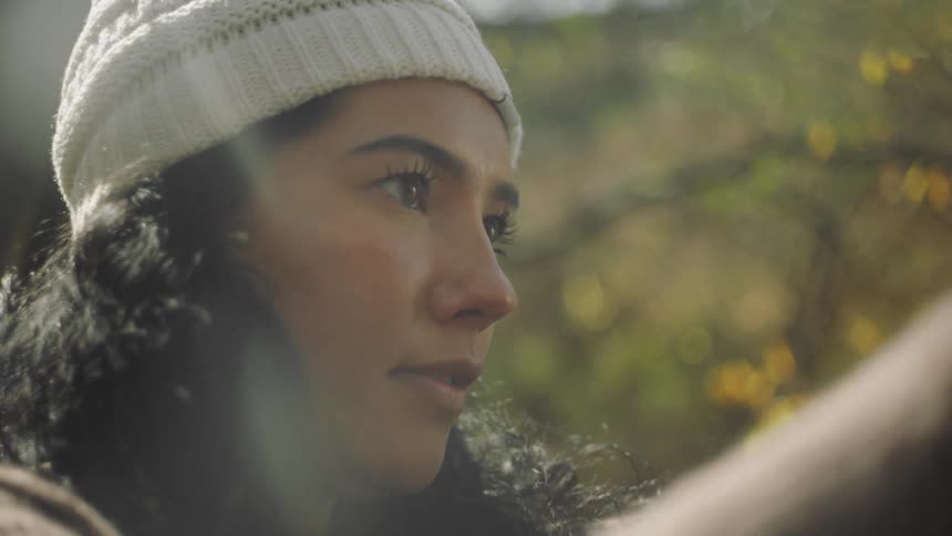 Woman wearing knit hat works outdoors near flowering plant