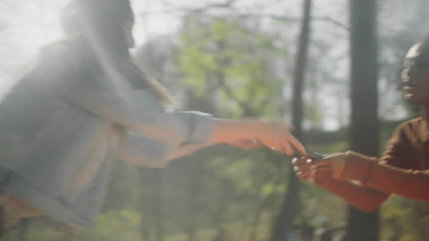 A woman hands a tent pole to a friend to put together at their camp site in the trees
