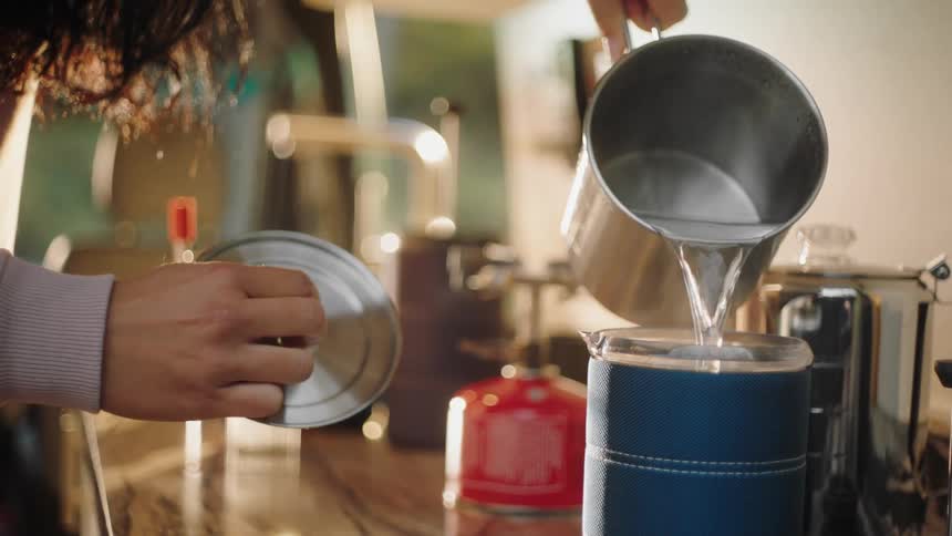 A woman pours hot water from a kettle into a french press
