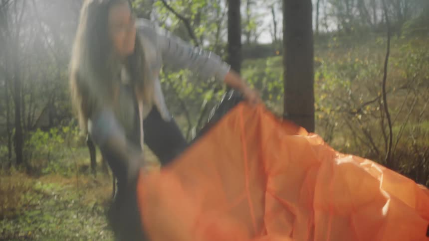 Two women laugh as they shake out a large orange tent while camping