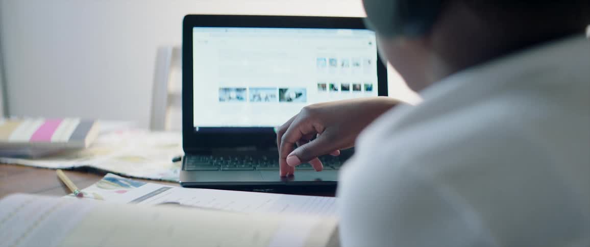 A boy with headphones sitting by a table with books using a laptop