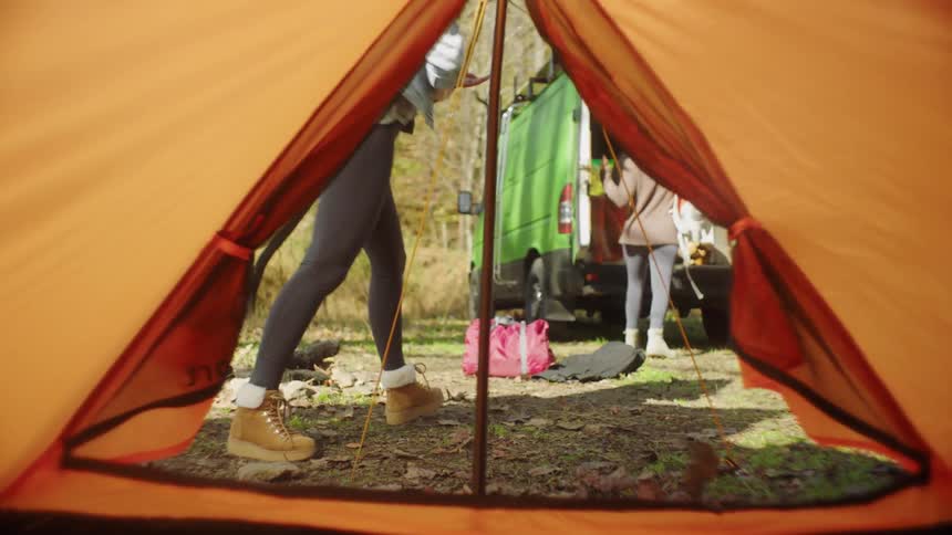 A woman setting up an orange tent while camping in nature
