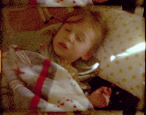 A young girl lying in a crib yawns and wipes her eyes as she notices she is being filmed