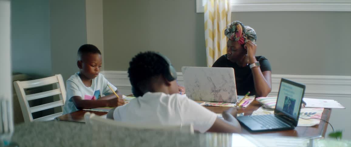 Mother helping her sons with homework on the dinner table in the kitchen at home