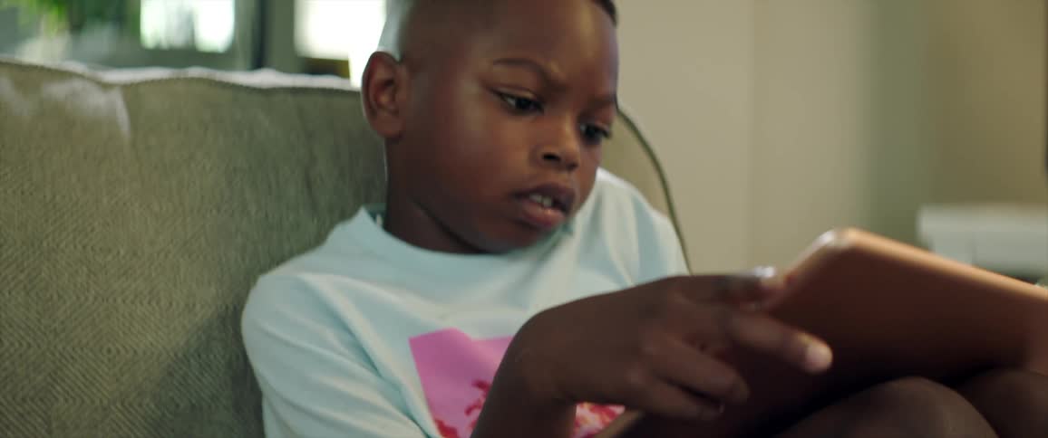 A young boy sits at home and looks at a tablet