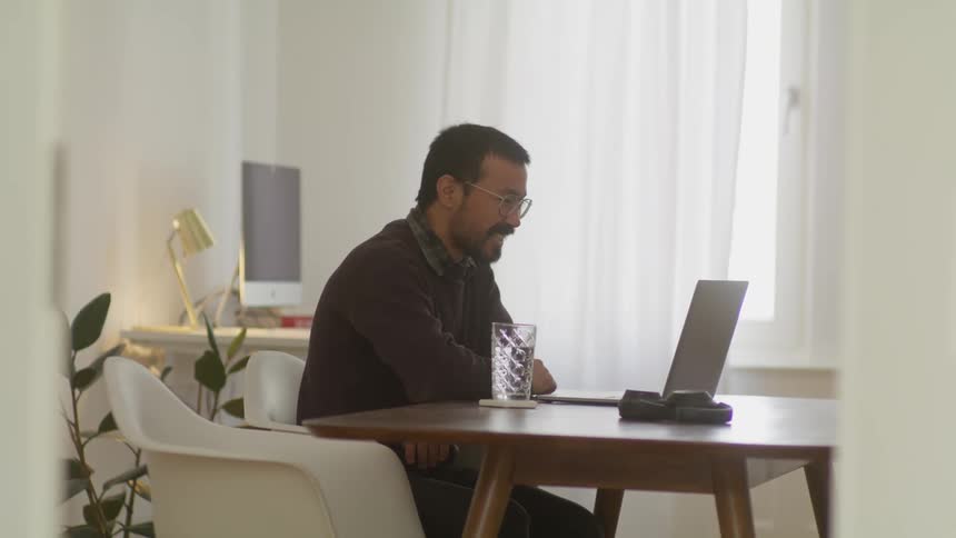 A man sits at a table and blows a kiss at someone hes talking to on his laptop