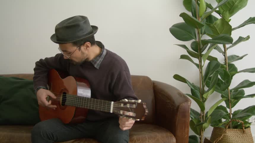 A guitarist tunes a guitar while sitting on a leather sofa indoors