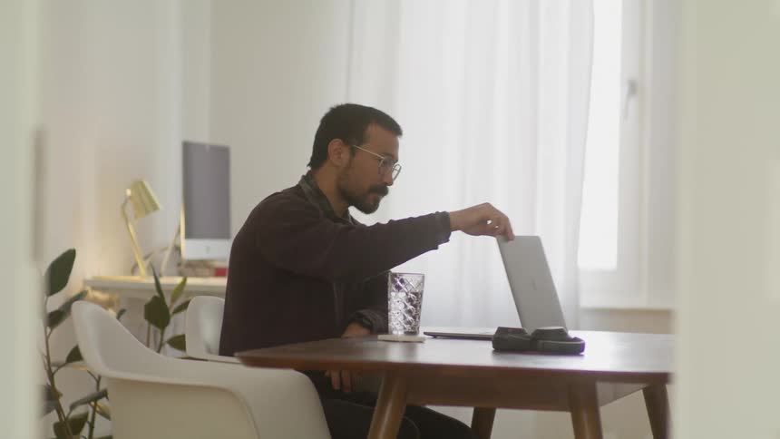 A man waves to the laptop then walks out of the room