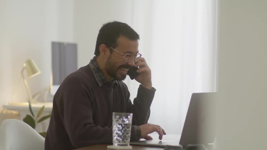 A man is sitting in an office and talking on a phone