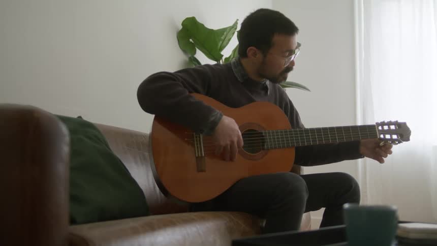 A man sits on a couch at home and plays the guitar