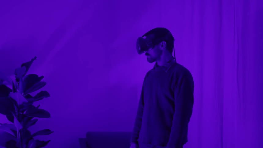 Man wearing virtual reality goggles standing in a room flooded with magenta lights