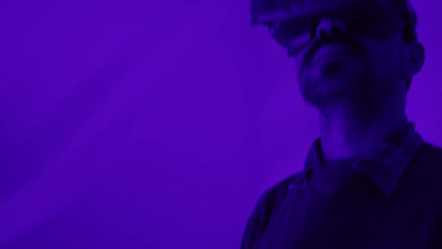 A man with a vr headset in a room with purple lights and a plant in the background