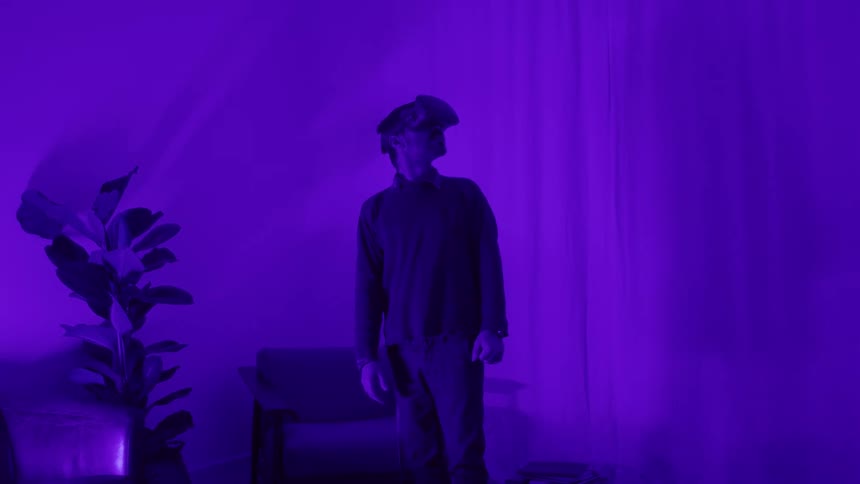 A man with a vr headset in a room with purple light with a wall and a plant in the background