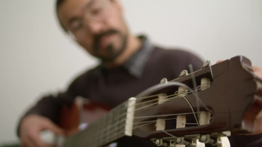 Man with beard and glasses plays and strings guitar
